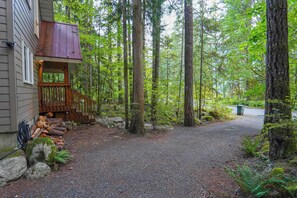 A house with a wooden deck and a gravel driveway leading to a forested area. - Cedar Hollow Mt Baker Cabin with Hot Tub and Stone Fireplace (Deming)