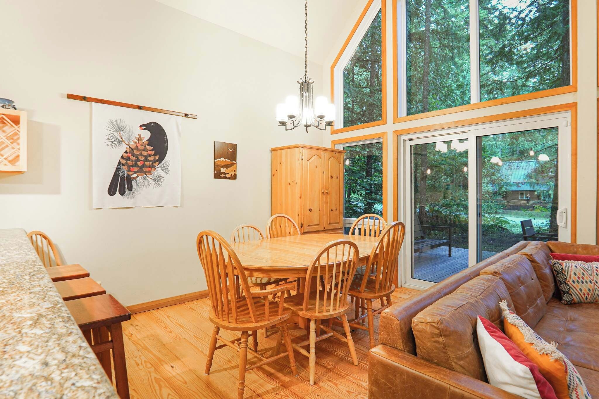 A dining area with a wooden table and chairs, a wooden cabinet, and a large window with a view of trees.