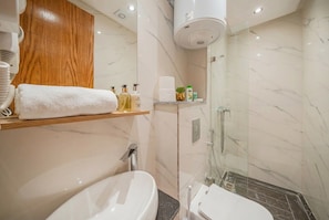Et stilfuldt badeværelse med et marmorvaskeskab, en brusekabine med glasvægge og et toilet.