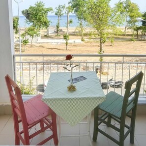 A balcony with a table and chairs, overlooking a beach with trees and a clear sky.