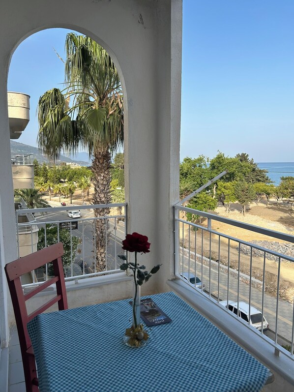 A balcony with a checkered table, a red rose, and a view of the sea and palm trees.