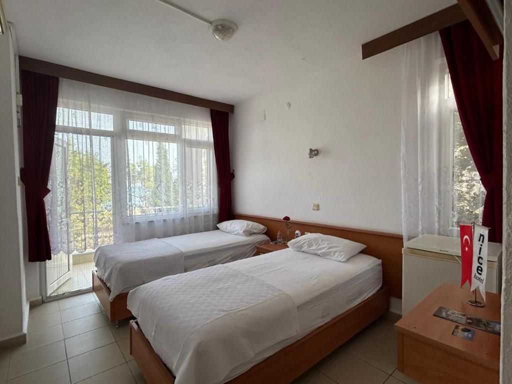 Et hotelværelse med to enkeltsenge, et lille bord med et rødt flag og et vindue med gardiner.