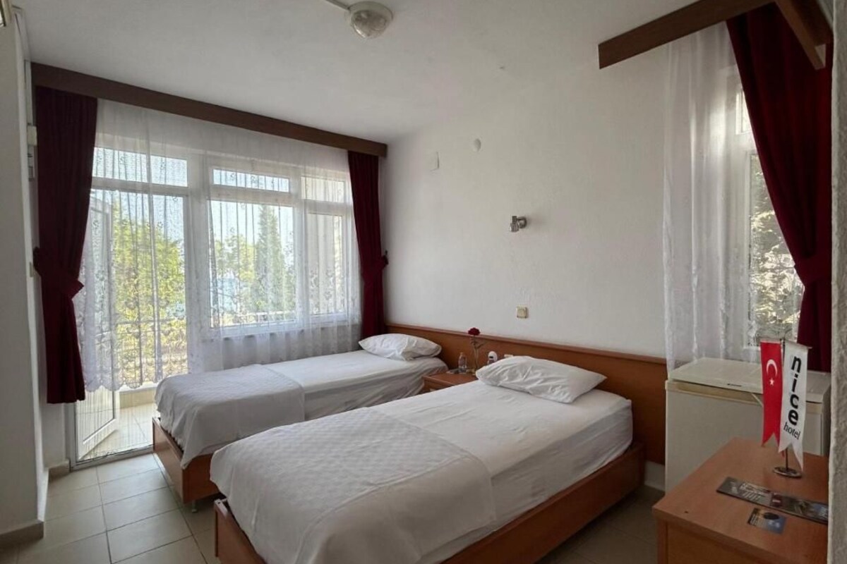 A hotel room with two single beds, a small table with a red flag, and a window with curtains.