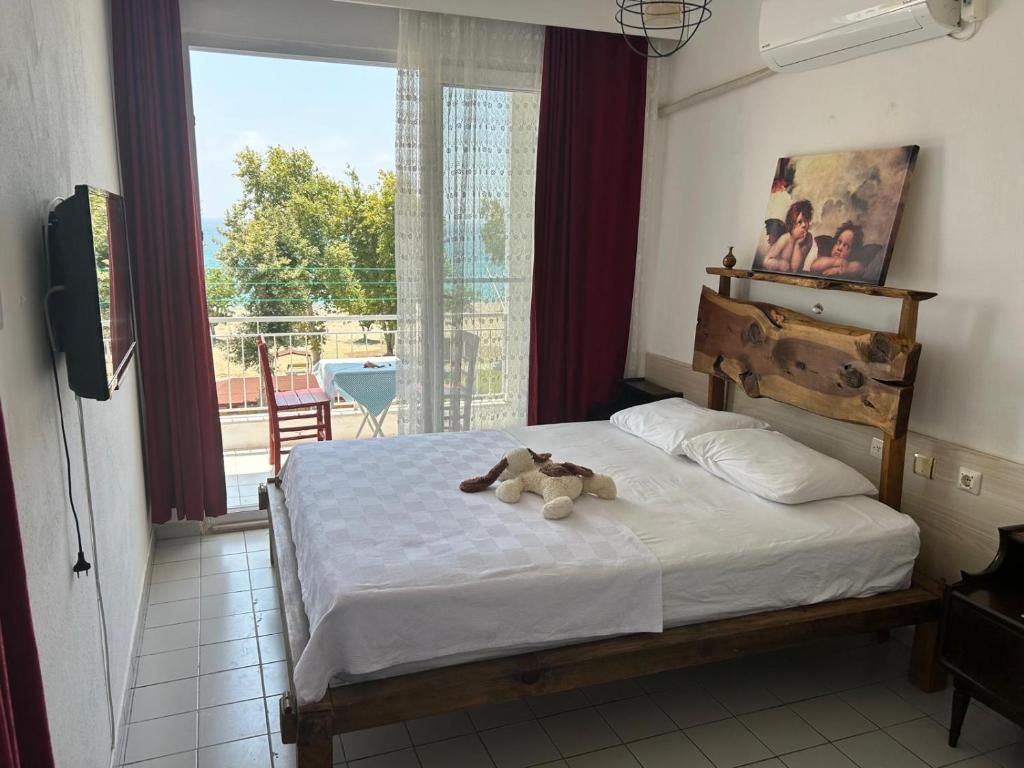 Quarto com cama, quadro, cabeceira de madeira, televisão e vista para o exterior.