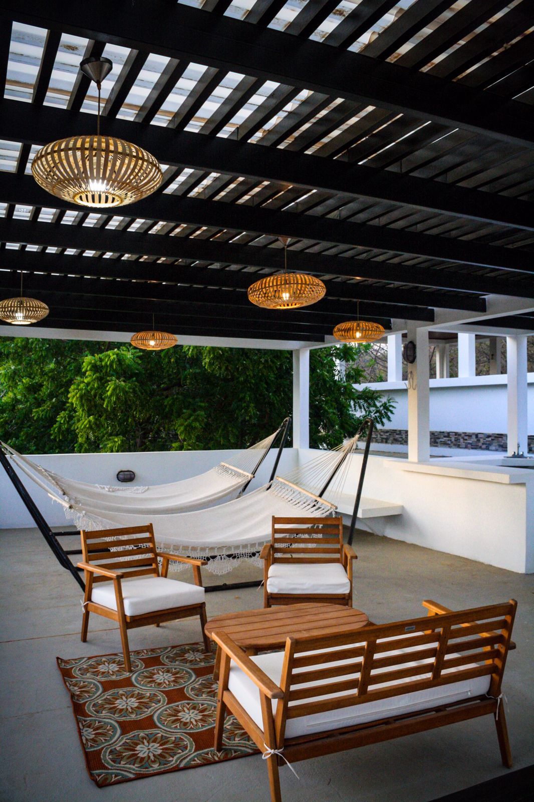 A hammock and wooden furniture under a covered area with a view of greenery.