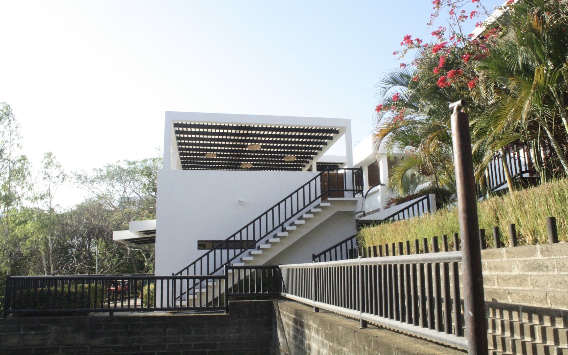 Un bâtiment moderne avec un escalier menant à un étage supérieur blanc, entouré de verdure et sous un ciel dégagé.