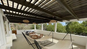 Un espace extérieur abrité, aménagé avec un hamac, des chaises en bois et une table.