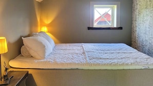 Una cama individual con cabecera, una lámpara de noche y una mesita con una figurita.