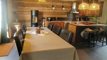 Een eetgedeelte met een lange tafel, meerdere stoelen en hangende rieten lampen.