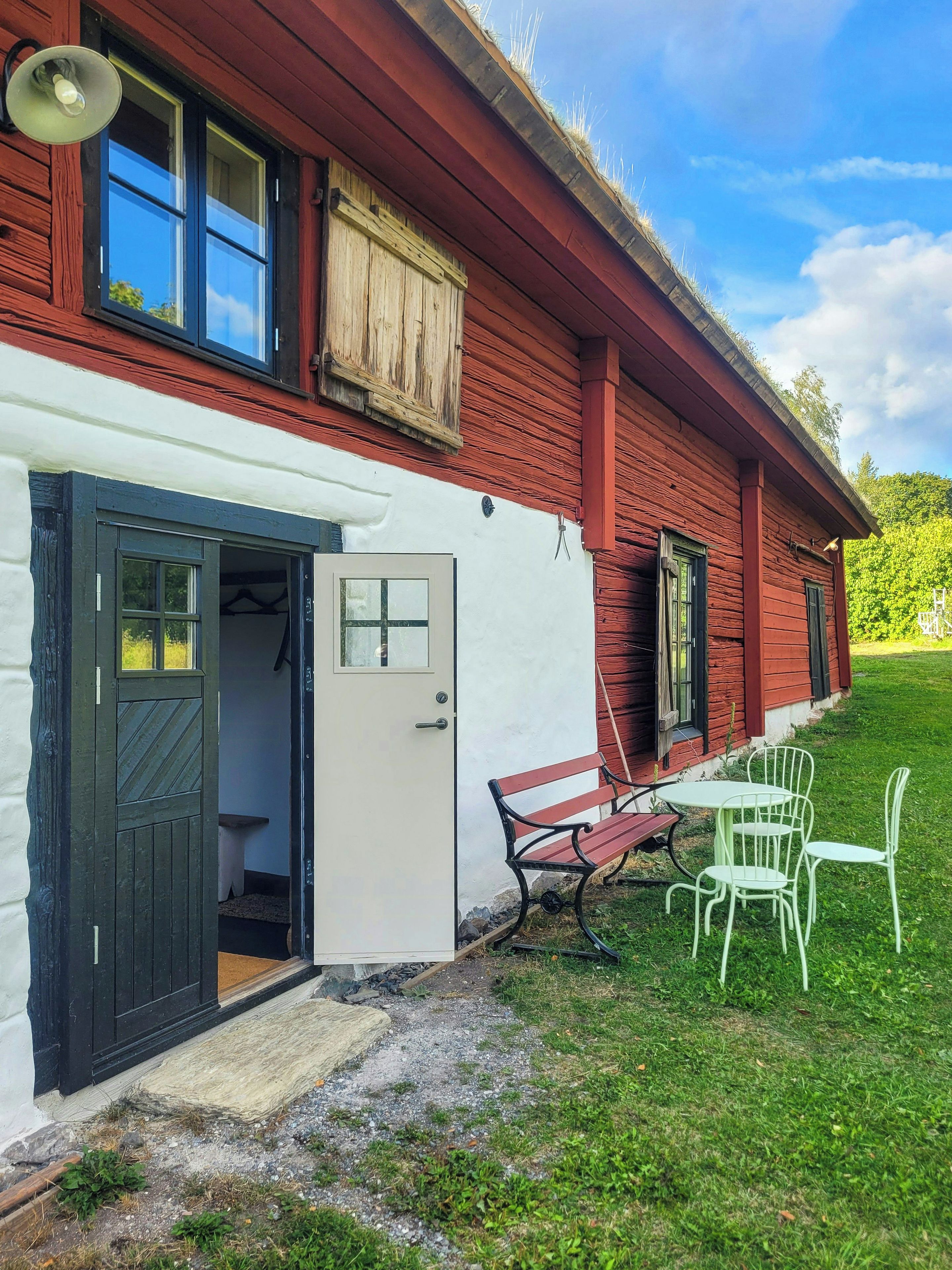 A red wooden house with a white exterior, a door, a bench, and a table with chairs.