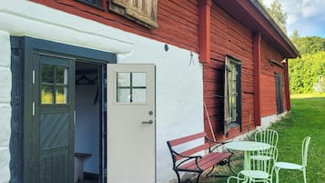 Een rode houten woning met een witte gevel, een deur, een bankje en een tafel met stoelen.