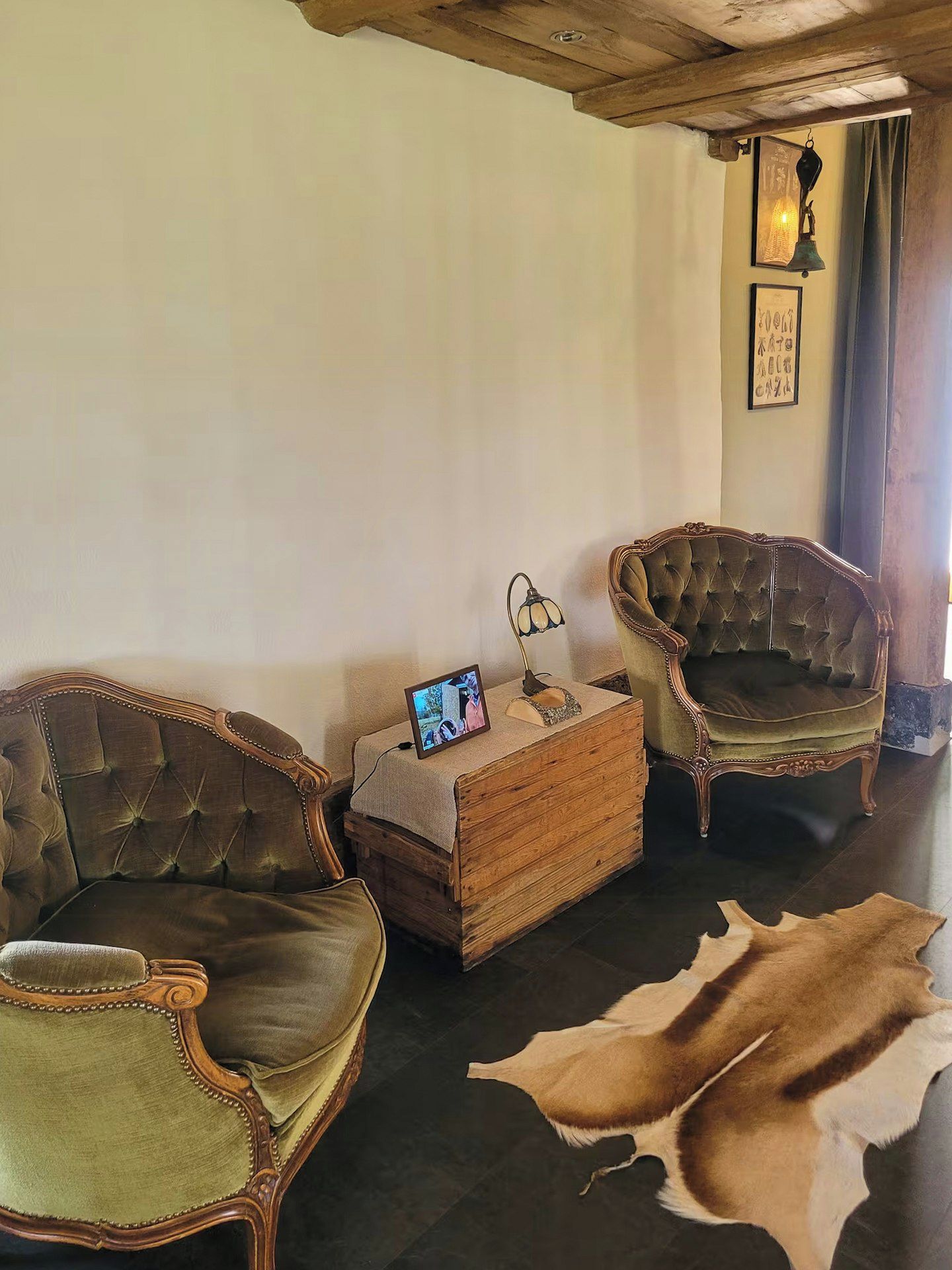 Een kamer met twee gestoffeerde fauteuils, een houten bijzettafeltje met een lamp, een televisie en een ingelijste foto aan de muur.