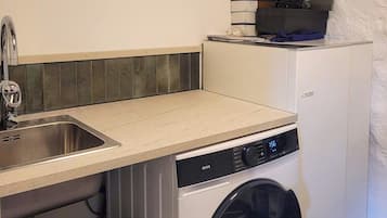 Een kleine keuken met een wasmachine, een spoelbak en een klein aanrecht.
