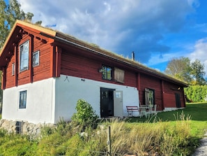 A red and white cabin with a stone foundation, a chimney, and a small porch with chairs. - Converted barn with grass roof in Lindesby (Nora)
