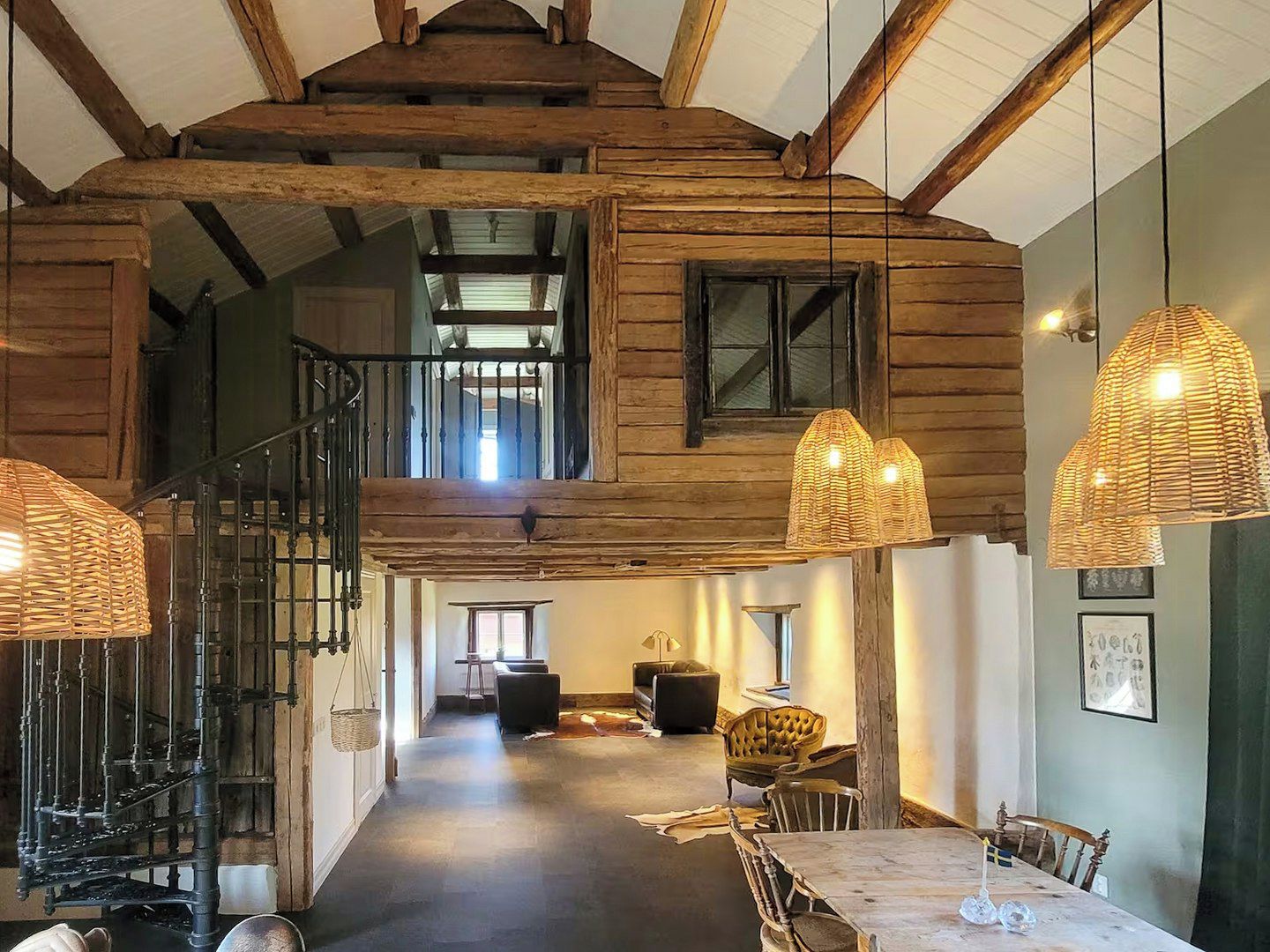 Un interior espacioso con techo alto, vigas de madera, una escalera y un comedor con mesa y sillas.