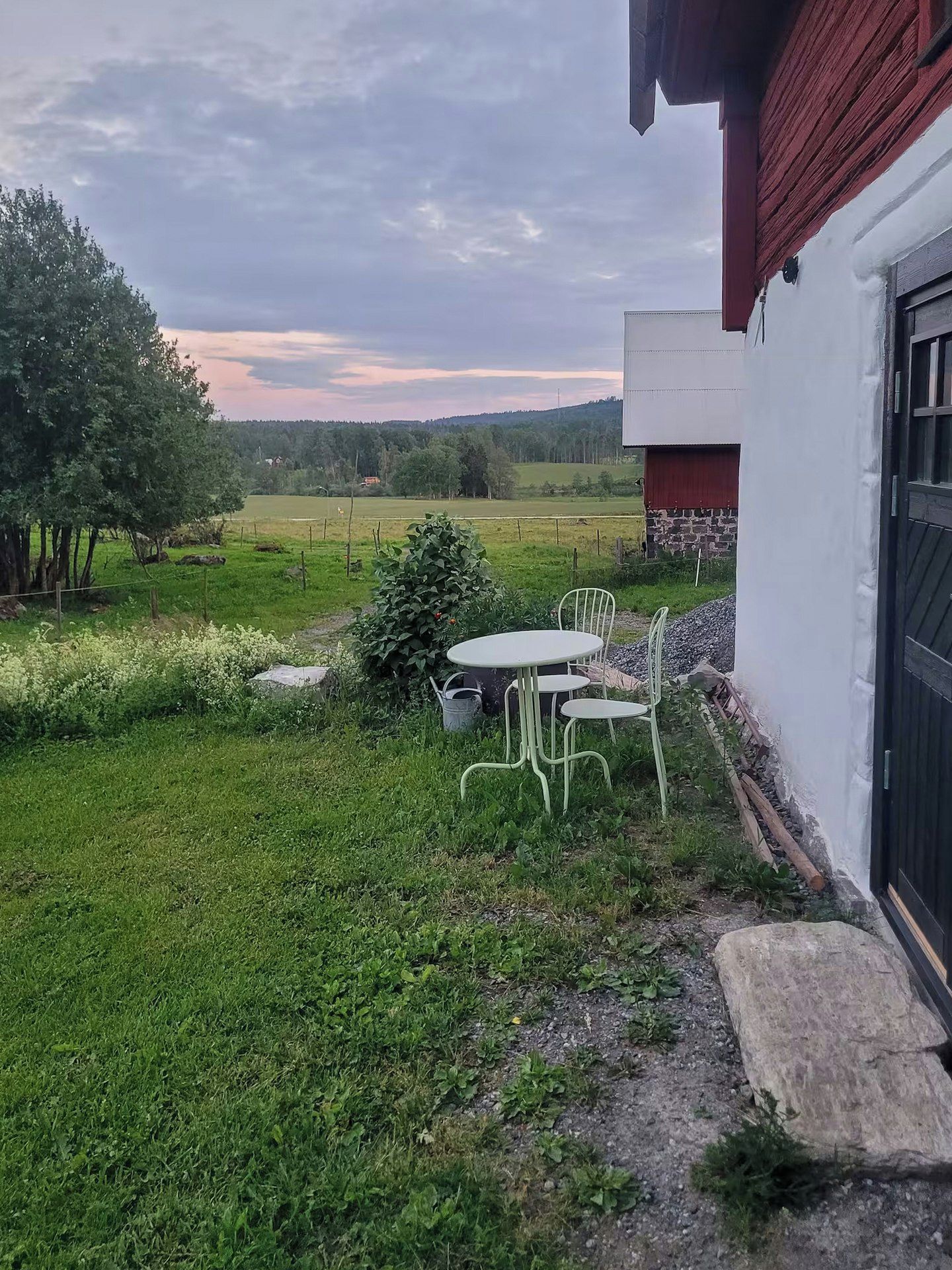Une terrasse avec une table et des chaises, un chemin de pierres et une vue sur un champ et des arbres.