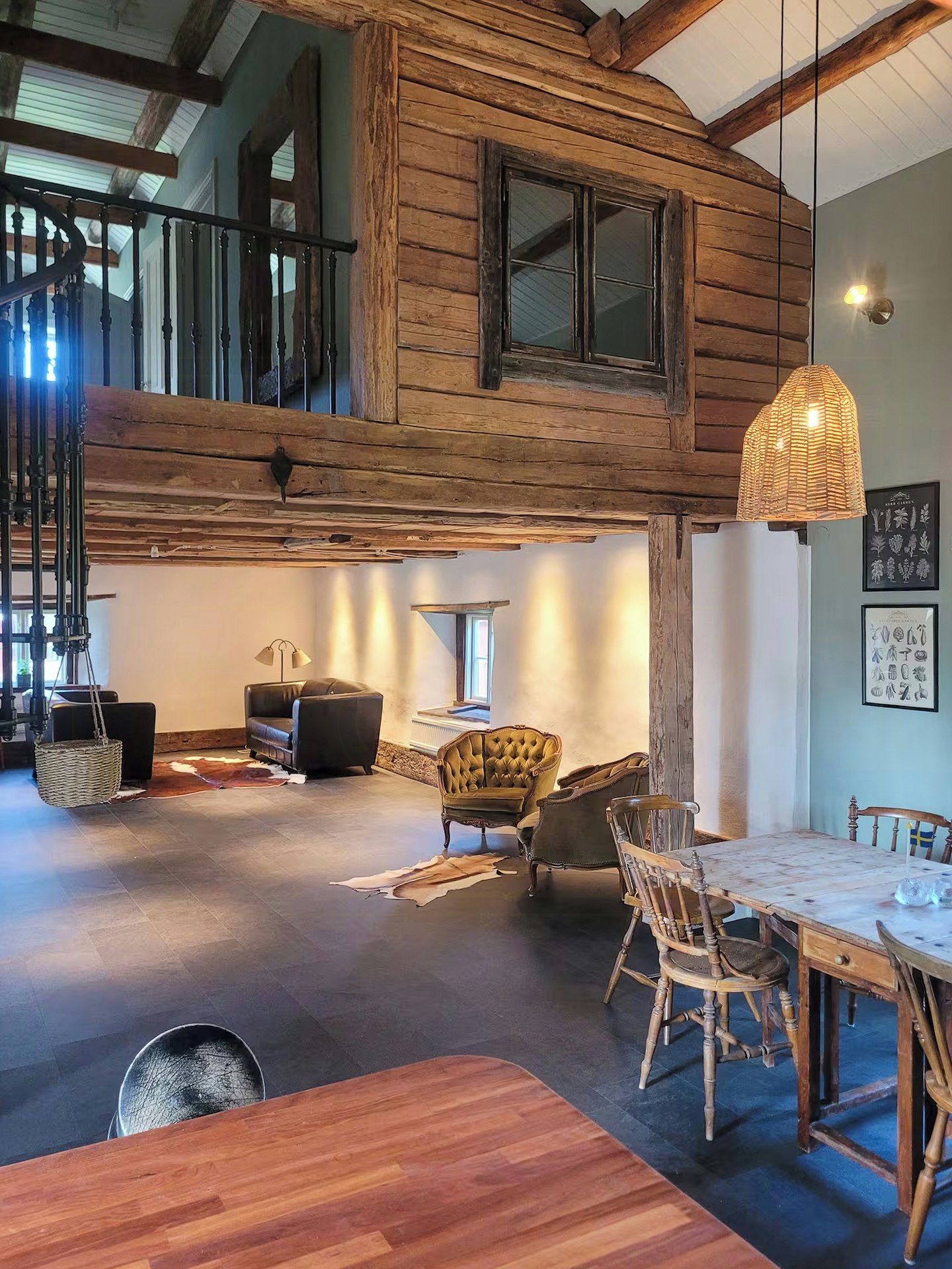 Un loft espaiós amb bigues de fusta a la vista, una zona de menjador amb taula i cadires de fusta, i un racó agradable amb sofà i butaques.