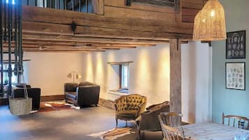 Un loft espaiós amb bigues de fusta a la vista, una zona de menjador amb taula i cadires de fusta, i un racó agradable amb sofà i butaques.