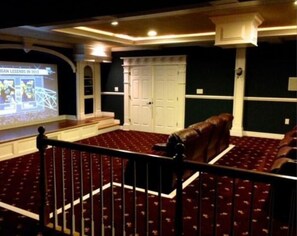 Ein Theater mit roten Teppichsitzen, einer Leinwand mit einer Präsentation und einer weißen Tür im Hintergrund.