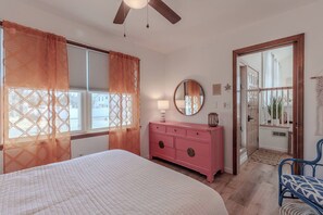 A bedroom with a bed, a pink dresser, a round mirror, and a ceiling fan. - Bleu Bay Cottage•Steps to Beach•Sleeps 8•Bay Views (Lower Township)