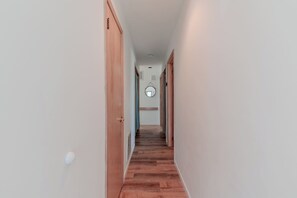 A narrow hallway with wooden flooring and white walls, leading to a room with a circular mirror on the wall. - Bleu Bay Cottage•Steps to Beach•Sleeps 8•Bay Views (Lower Township)
