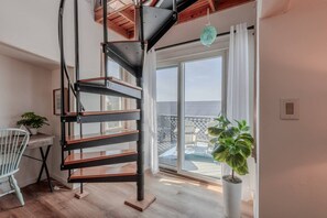 A modern interior with a spiral staircase, a balcony with a view, and a potted plant. - Bleu Bay Cottage•Steps to Beach•Sleeps 8•Bay Views (Lower Township)