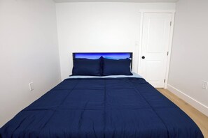 A bedroom with a bed, a door, and a wall with a light switch. - Salt Air Cottage•Pet Friendly•Fire Pit•EV Charger• (Lower Township)