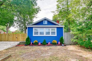 A single-story house with a blue exterior, a front porch, and a small garden with flowers and two American flags. - Salt Air Cottage•Pet Friendly•Fire Pit•EV Charger• (Lower Township)
