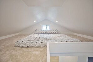 A bedroom with a sloped ceiling, a single bed with patterned bedding, a window, and a carpeted floor. - Salt Air Cottage•Pet Friendly•Fire Pit•EV Charger• (Lower Township)