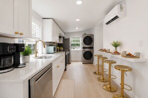 A modern kitchen with a coffee maker, washing machine, and bar stools. - Salt Air Cottage•Pet Friendly•Fire Pit•EV Charger• (Lower Township)