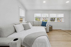A modern bedroom with a large bed, a sofa, and a window with blinds. - Salt Air Cottage•Pet Friendly•Fire Pit•EV Charger• (Lower Township)