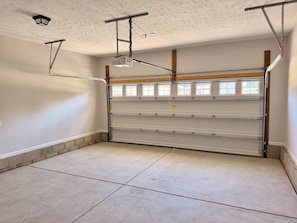 A garage with a metal door, ceiling lights, and a window with blinds.