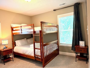 A bunk bed with a wooden frame, a bedside table with a lamp, and a window with curtains.