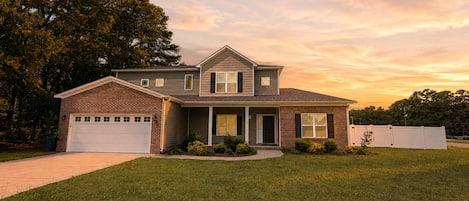 A two-story house with a brick garage, a covered front porch, and a well-maintained lawn.