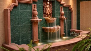 Una fuente de varios niveles y un emblema central, frente a una pared de mármol verde con un arco decorativo.