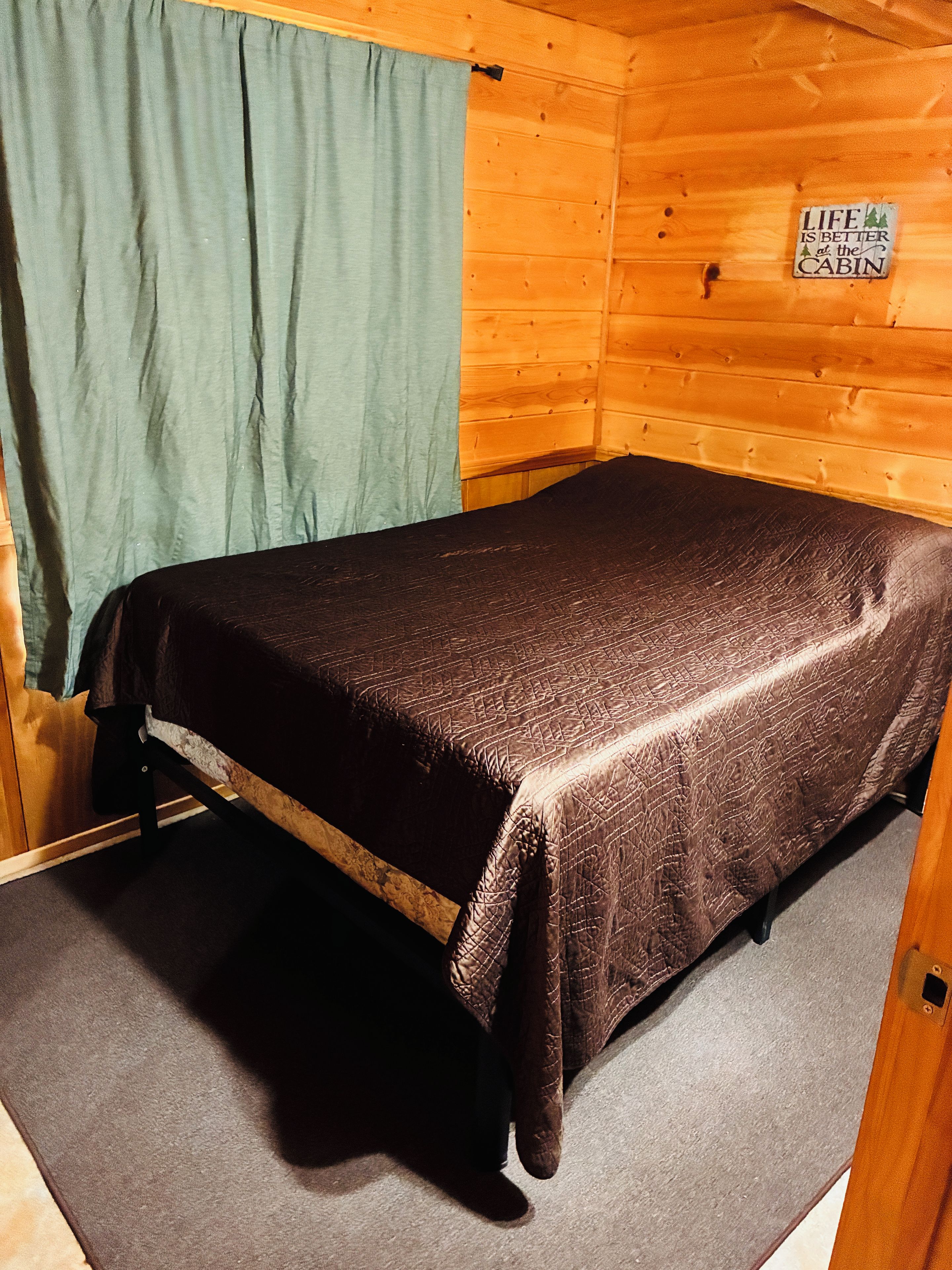 A single bed in a cabin with a wooden wall and a sign that says 'Life is better at the cabin.'