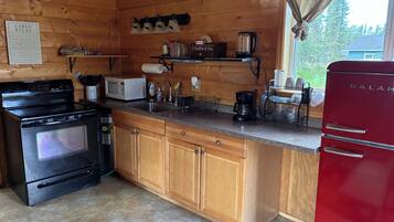 A cabin kitchen with wooden cabinets, a black stove, a microwave, a coffee maker, and a red refrigerator.