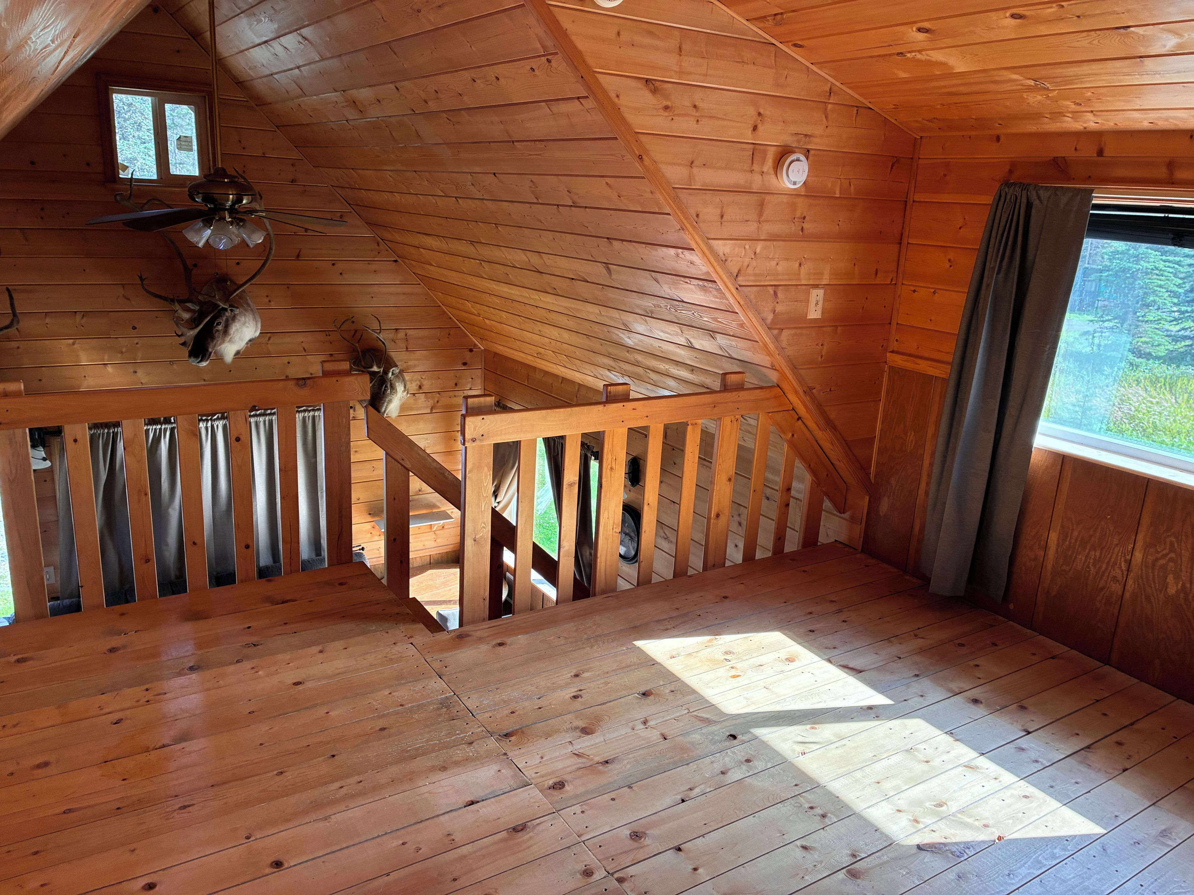 A wooden interior with a sloped ceiling, a staircase, and a window with curtains.
