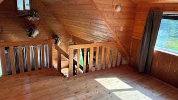 A wooden interior with a sloped ceiling, a staircase, and a window with curtains.