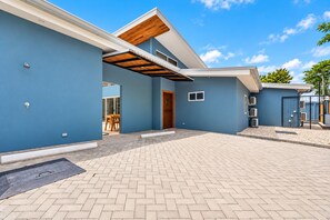 Une maison moderne dotée d’un patio couvert, d’une porte en bois et surplombée d’un ciel bleu azur.