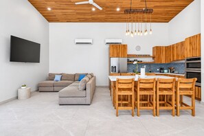 A modern living room with a sofa, a flat-screen TV, and a dining area with wooden chairs and a table. - Casa Carlayna - tranquil villa in Potrero. Pool/Cool water Jacuzzi, WiFi, AC. (Potrero)