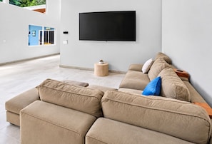 A modern living room with a beige sectional sofa, a flat-screen TV mounted on the wall, and a small wooden side table. - Casa Carlayna - tranquil villa in Potrero. Pool/Cool water Jacuzzi, WiFi, AC. (Potrero)