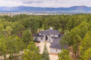 Une grande maison entourée d’une forêt dense de pins, avec vue sur des montagnes lointaines.