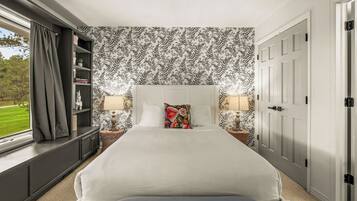 A bedroom with a large bed, two bedside tables with lamps, a bookshelf, and a window with curtains.