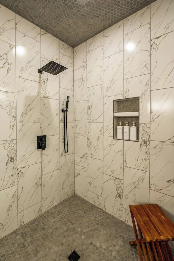 A shower area with a marble wall, a handheld showerhead, and a shelf with toiletries.