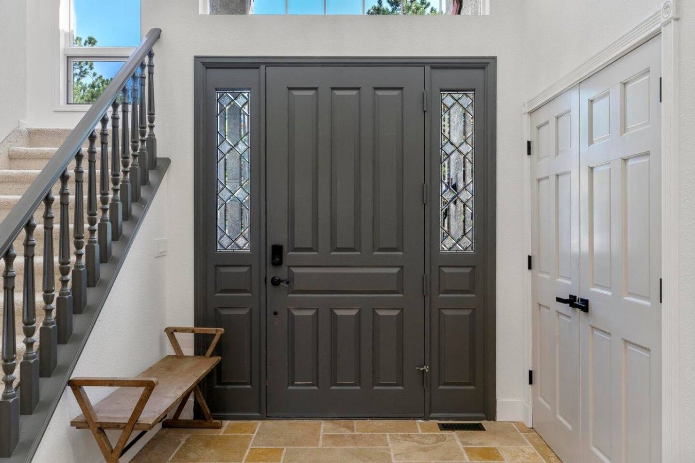 A grey double door with a small bench in front, a staircase to the left, and a white door to the right.