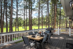 A deck with a table and chairs, overlooking a golf course.