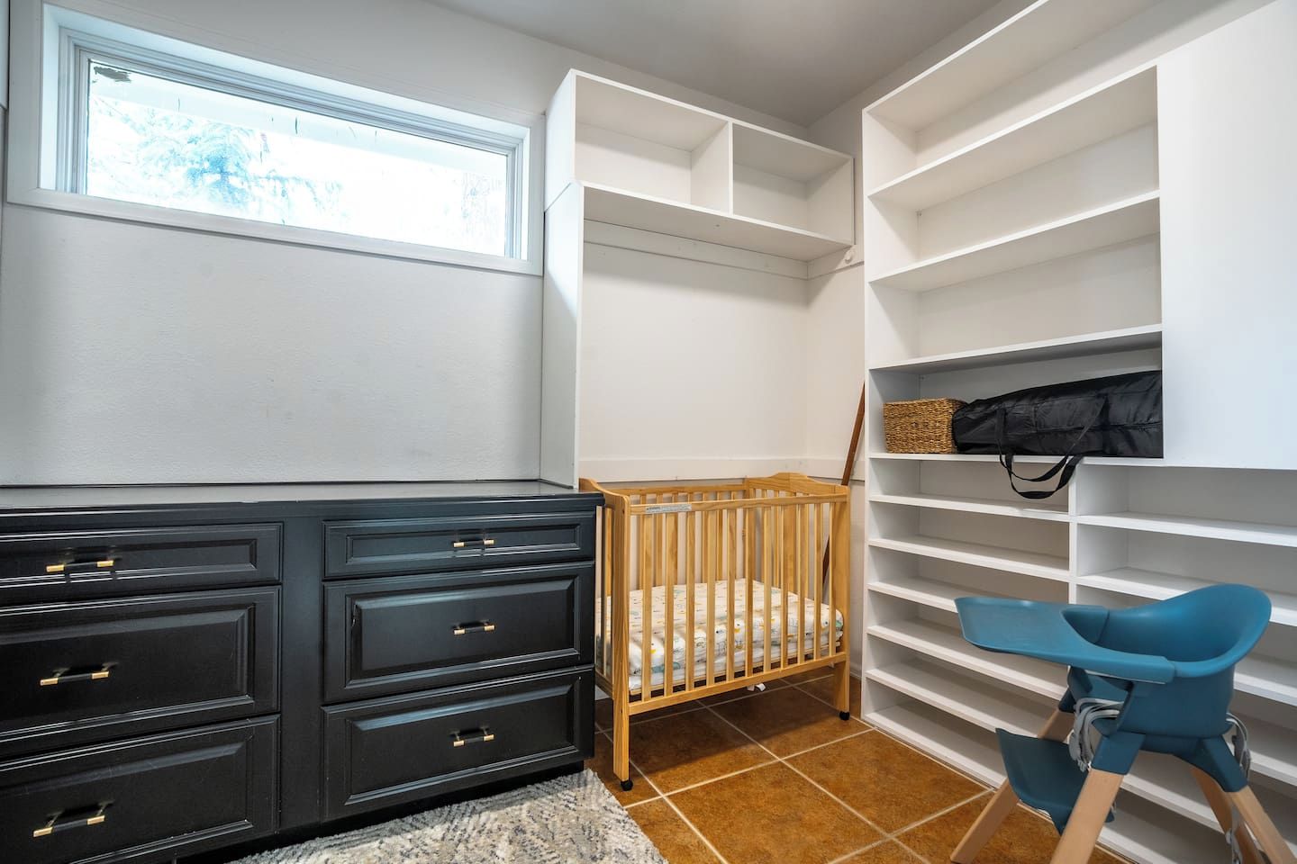Habitación con cuna, cómoda y silla. Hay estantes con espacio de almacenamiento.