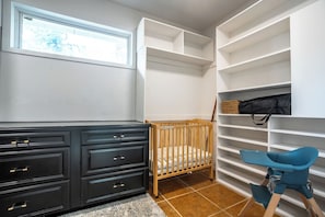 A room with a crib, a dresser, and a chair. There are shelves with storage space.
