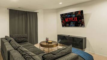 A living room with a sectional sofa, a coffee table, a flat-screen TV mounted on the wall, and a dark-colored entertainment unit.